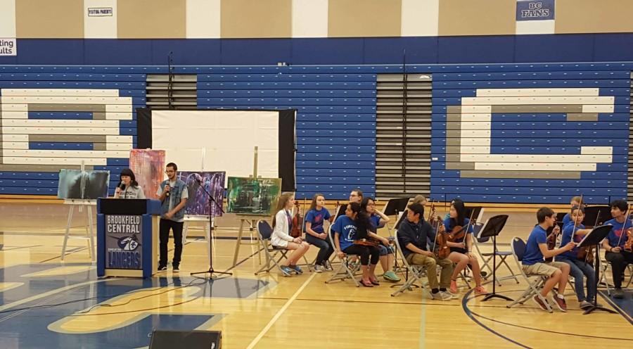Abby Ng (‘16) and Dalton Errath (‘16) present during the assembly as the orchestra looks on.