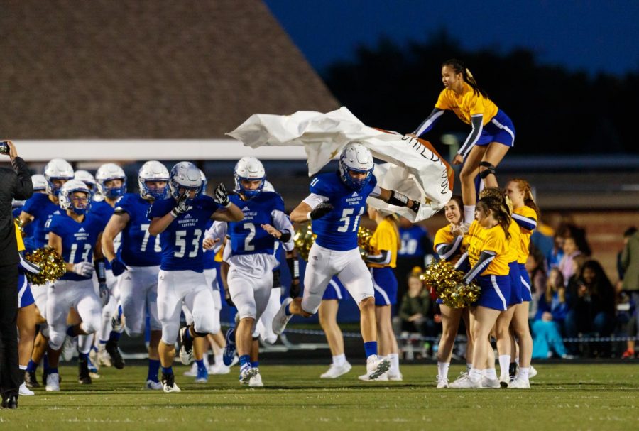 Cheerleaders, Tirzah Sonderman (20), and Ainsley Regner (22) hold up a banner made by the cheer team for the football team to run through. Captains Alec Mejchar (19), Chris Casey (19), Drew Lescznski (19) run through first. This was the first year the cheerleaders made a banner, but the cheerleaders hope to eventually make it a tradition. 