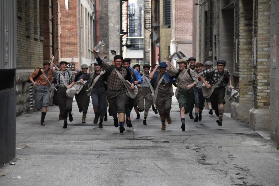 The Newsies cast runs towards the camera while taking cast photos. The cast performed at the Holiday Kickoff with the marching band and choir.